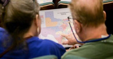 Two attendees seated close together examine a printed map of proposed Texas congressional districts during a public hearing.