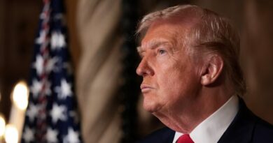 Donald Trump appears in profile, looking serious, with a US flag blurred in the background.