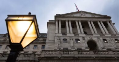 The Bank of England building with columns and statues, viewed from below, with a lit streetlamp in the foreground.