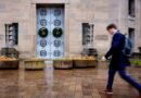The entrance of the Robert F Kennedy Department of Justice Building with two wreaths on the doors and a person walking past.