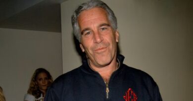 Jeffrey Epstein stands indoors at the launch of Radar Magazine, wearing a dark zip-up top with red initials.