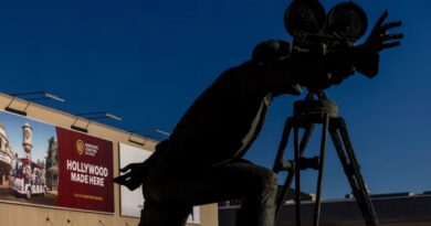 A statue of a film director with a camera stands in front of a Warner Bros Studio Tour billboard reading Hollywood Made Here.