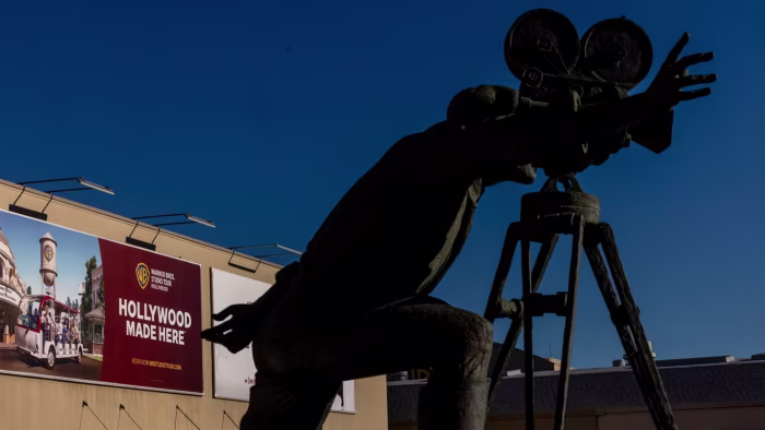 A statue of a film director with a camera stands in front of a Warner Bros Studio Tour billboard reading Hollywood Made Here.