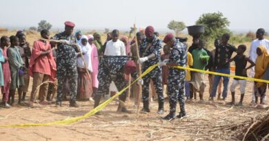 Nigeria police Anti-Bomb squad officers secure an area with yellow tape as a crowd of local residents observes.