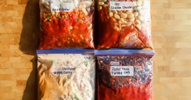 Four labeled freezer bags filled with homemade meals&mdash;beef stew, Italian chicken, chickpea veggie curry, and taco turkey chili&mdash;arranged on a wooden surface.