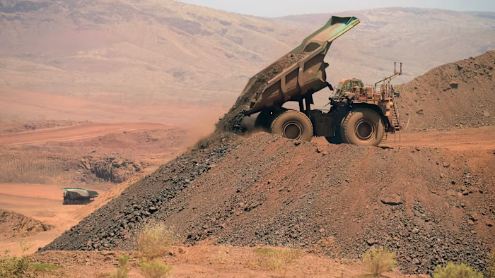 An autonomous haul truck unloads a pile of rock at a mining site, with another haul truck visible in the background.