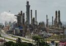 PDVSA El Palito refinery with multiple smokestacks emitting white smoke and industrial structures surrounded by greenery.