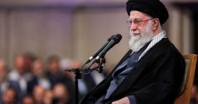 Ayatollah Ali Khamenei speaks into two microphones while seated, with a blurred audience in the background.