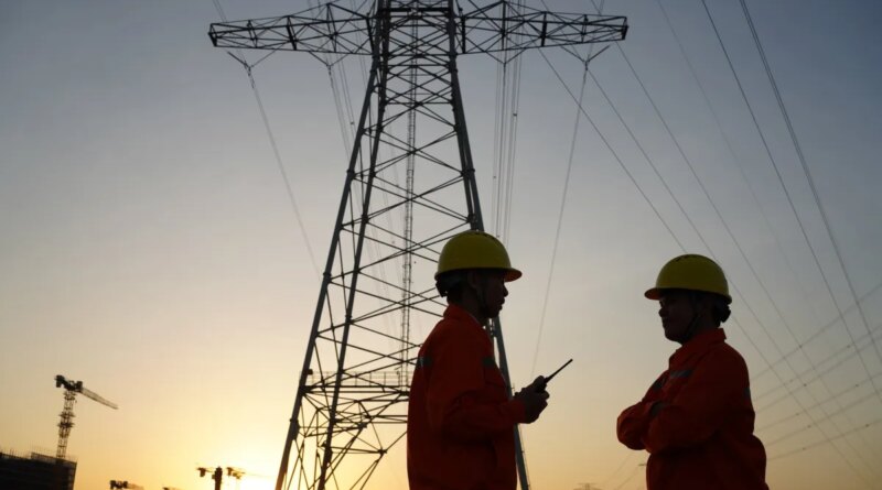 Two workers inspect high-tension power lines.