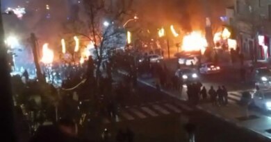A blurry image of a dark street filled with fires, cars and people.
