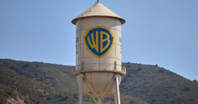 The Warner Bros. Studios water tower with the WB shield logo, set against hills and a clear sky.