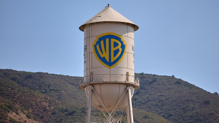 The Warner Bros. Studios water tower with the WB shield logo, set against hills and a clear sky.