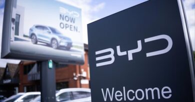 A BYD showroom sign in the foreground with a billboard showing a BYD car and the words "Now open" in the background.