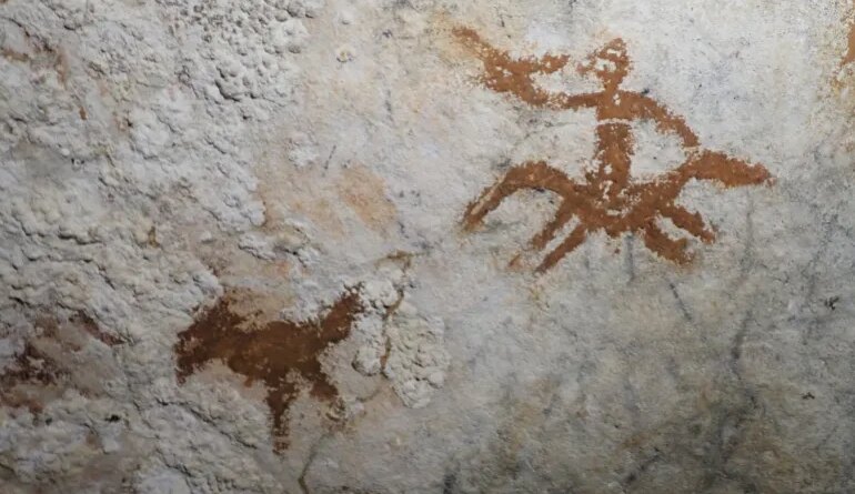 This image provided by Maxime Aubert shows cave drawings in Sulawesi, Indonesia of a human figure and a bird with a faded handprint in between them. (Maxime Aubert via AP)