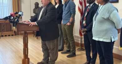 Mark Dion speaks at a podium, surrounded by city officials