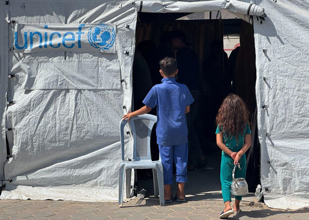 On 26 September 2025, children stand outside a tent being used for medical services at Al Aqsa Hospital in Deir al Balah in the Gaza Strip. Credit: UNICEF/James Elder