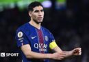 Achraf Hakimi, wearing a blue and red Paris St-Germain shirt, holds out his arms