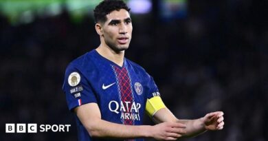 Achraf Hakimi, wearing a blue and red Paris St-Germain shirt, holds out his arms