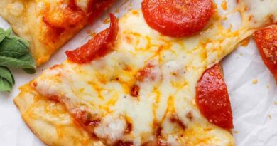 A hand holding a slice of pepperoni pizza with melted cheese on a white parchment background.