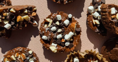 Chocolate treats topped with mini marshmallows, chocolate chips, and chopped nuts are arranged on a light textured surface.