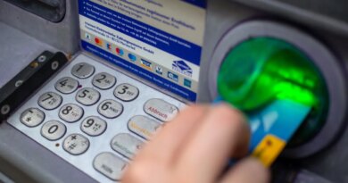 a close-up photo of a person punching in their PIN on an ATM in a wall.