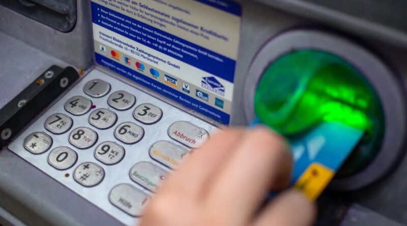 a close-up photo of a person punching in their PIN on an ATM in a wall.