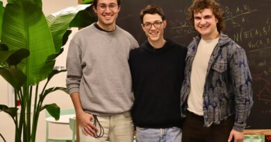 Three smiling men stand in front of a chalkboard