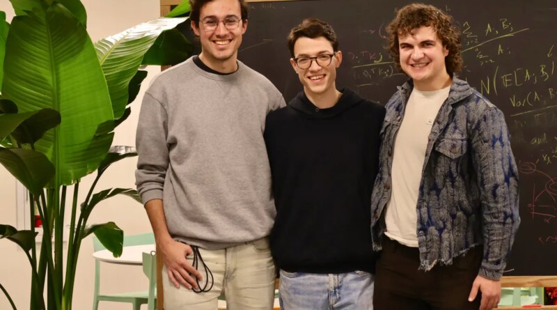 Three smiling men stand in front of a chalkboard