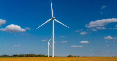 Two wind turbines stand against with a blue sky with cumulus clouds.