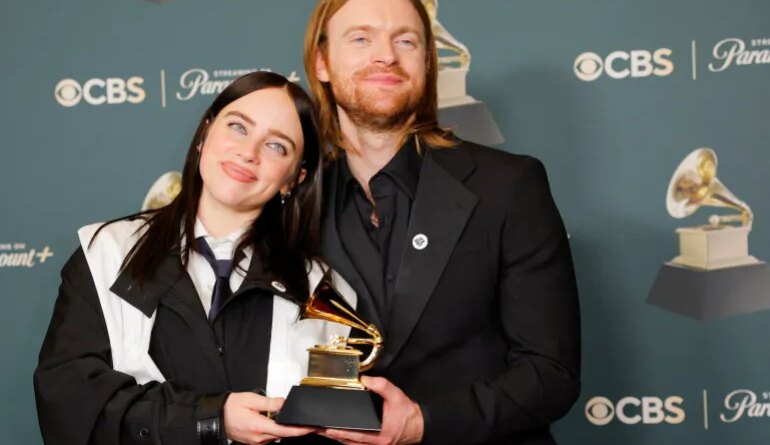 Billie Eilish and Finneas wearing ICE Out pins pose with the award for Song of the Year for "WILDFLOWER"