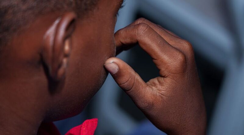 A close-up of a young boy in Haiti, his hand near his face, reflecting on the challenges of gang violence and the launch of the PREJEUNES programme to protect children from recruitment.