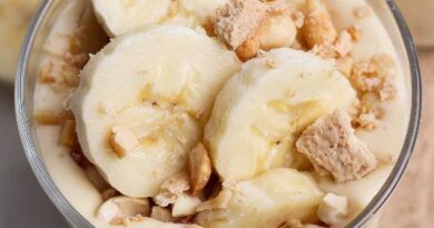 A glass bowl filled with banana pudding, topped with banana slices, chopped nuts, and crumbled cookies.