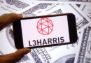The L3Harris Technologies company logo is seen displayed on a smartphone screen with dollars in the background.