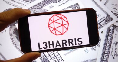 The L3Harris Technologies company logo is seen displayed on a smartphone screen with dollars in the background.