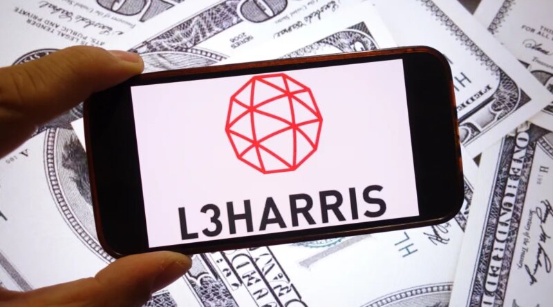 The L3Harris Technologies company logo is seen displayed on a smartphone screen with dollars in the background.