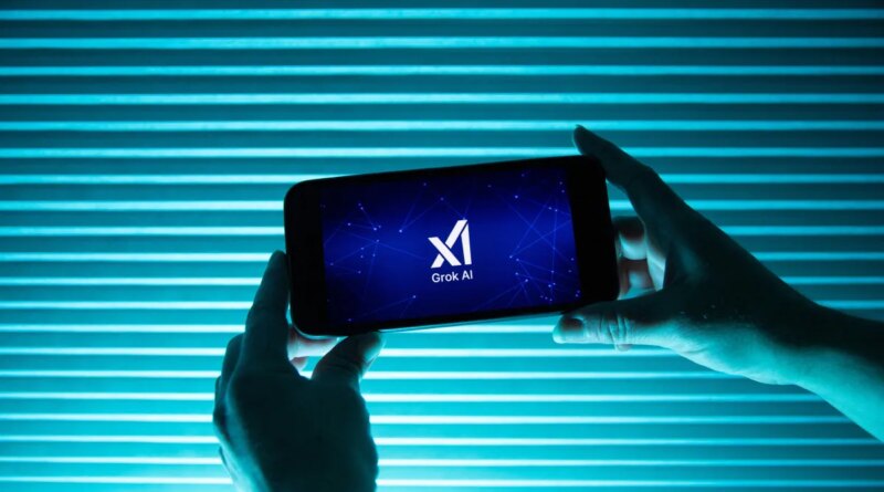 A person holds a telephone displaying the logo of Elon Musk s artificial intelligence grok in front of a background lit by a blue light.
