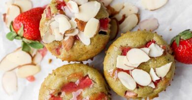 Three muffins with visible strawberry pieces and sliced almonds on top, placed on parchment paper with fresh strawberries and almond slices nearby.