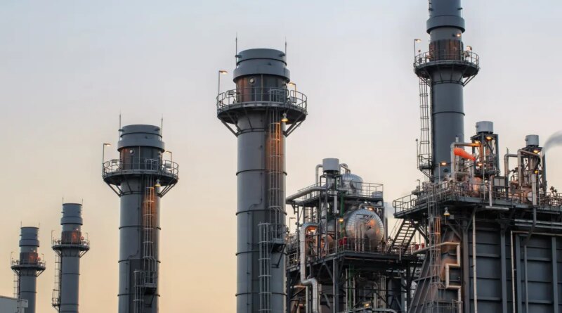 Natural gas power plant smoke stacks stand against a twilight sky.