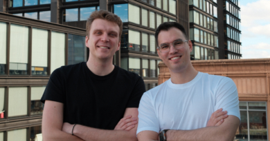 Two men stand on a rooftop, crossing their arms