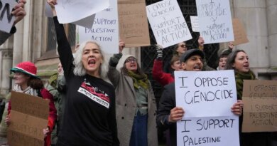 Protesters hold signs that read "I OPPOSE GENOCIDE" and "I SUPPORT PALESTINE ACTION." Many people have their mouths open as if shouting.