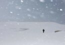 A man walking amid heavy snowfall covering sand dunes. 