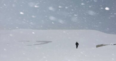 A man walking amid heavy snowfall covering sand dunes.