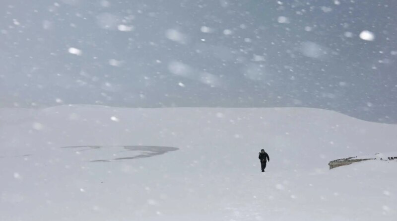 A man walking amid heavy snowfall covering sand dunes.