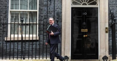 Keir Starmer, in a dark suit, carries a stack of folders as he walks in front of the black door of No. 10 Downing Street.