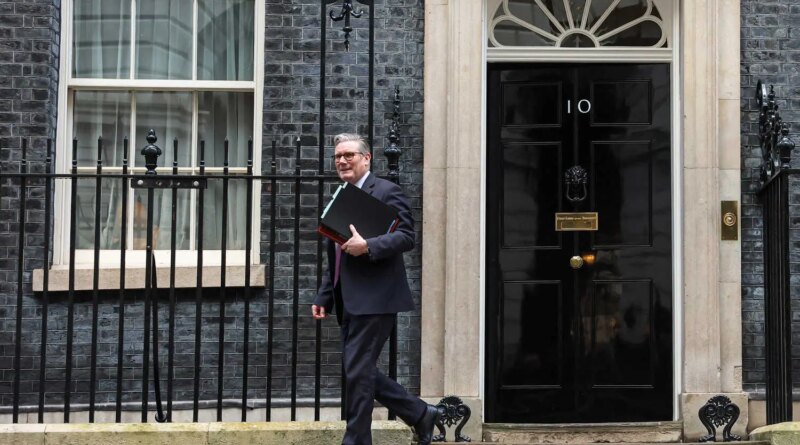 Keir Starmer, in a dark suit, carries a stack of folders as he walks in front of the black door of No. 10 Downing Street.