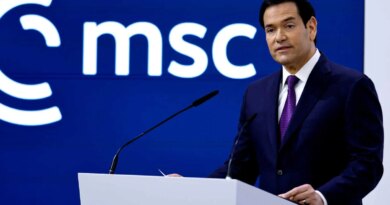 Marco Rubio, wearing a dark suit and a purple tie, stands at a white lectern with two microphones. A blue wall with a white “msc” logo is behind him.