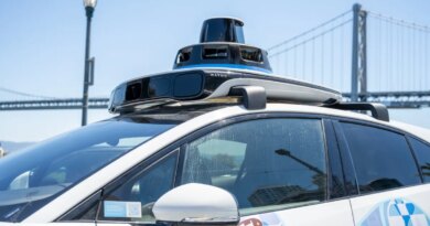 Self-driving Waymo car with rooftop lidar and bird-themed mural on the Embarcadero with the San Francisco-Oakland Bay Bridge in background, San Francisco, California, August 14, 2025.
