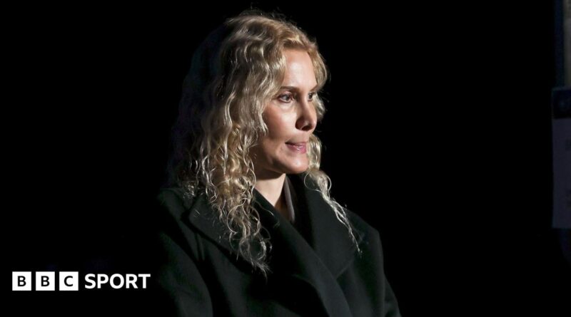 Blonde-haired coach Eteri Tutberidze in a black outfit against a black background