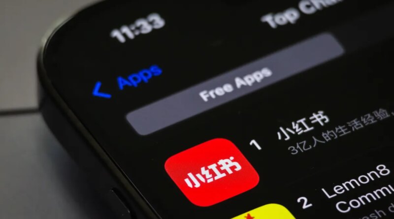 A smartphone screen displays the RedNote app (Xiaohongshu) ranking first in the Free Apps category on the App Store