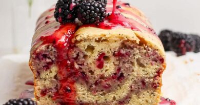A loaf of blackberry bread topped with blackberries and a drizzle of blackberry sauce.